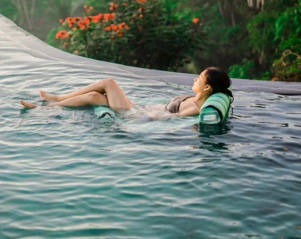 acquaboss hammock Person relaxing in a serene pool surrounded by greenery and vibrant flowers, representing a calm and natural environment.