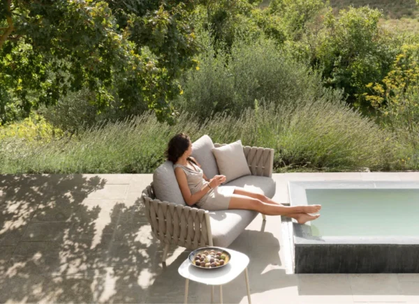 Outdoor sofa set with cushions by a poolside, placed in a lush garden.