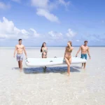 Group of people carrying an inflatable pool lounge mat along the beach, preparing for water fun