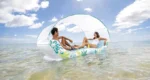 Two people relaxing on an inflatable water lounge with a canopy, floating on a calm water surface