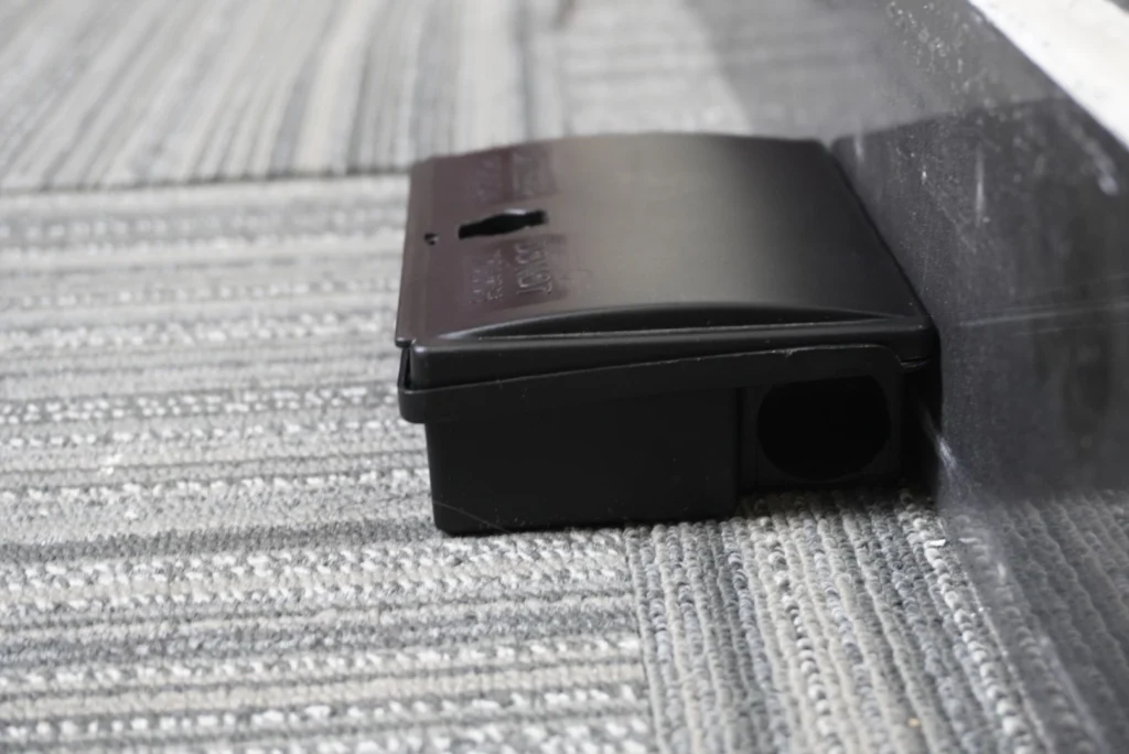 Small black mouse bait station with a sleek design, positioned on a textured surface, highlighting its discreet and secure rodent control features.