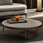 Round coffee table with a textured surface and metal legs, placed in a modern living room.