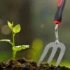 Gardening hand fork digging soil around a young plant seedling, showcasing effective soil aeration and preparation.