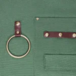 Close-up of We The Wild gardening apron showing metal ring and reinforced pockets for holding tools.